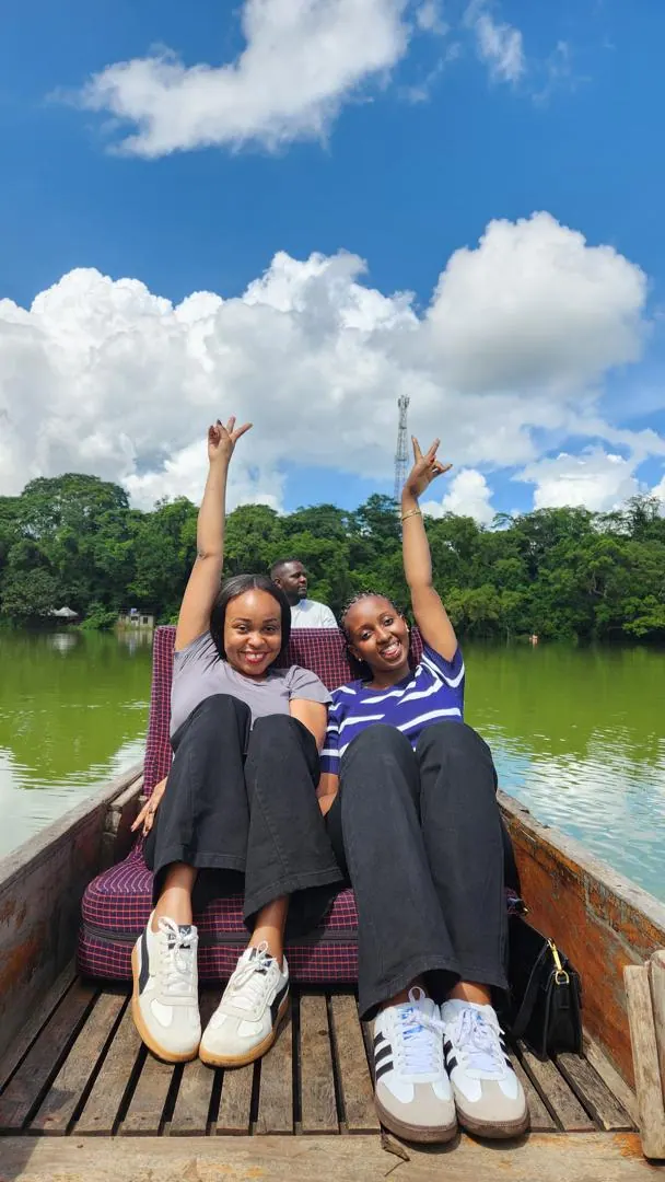 Two guests in a canoe on Lake Duluti with their arms raised under a blue sky